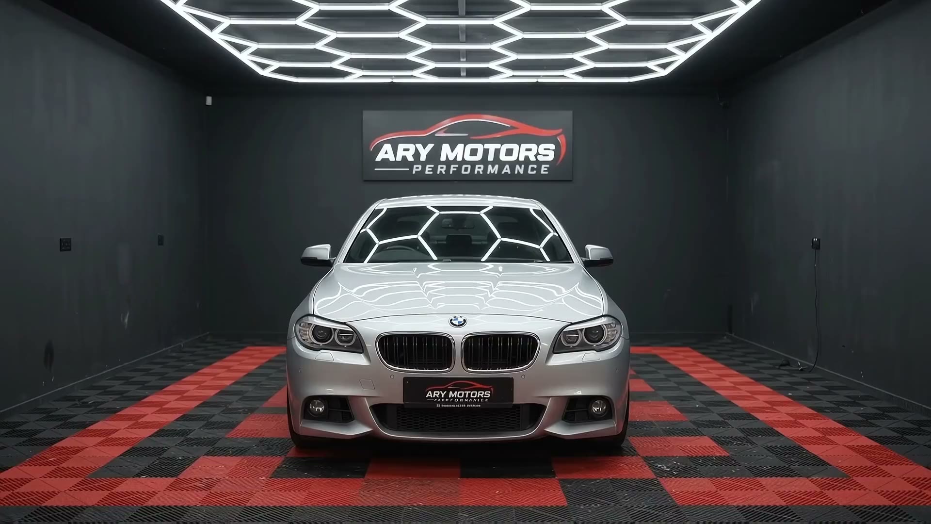 Silver BMW under hexagon lights on the red and black chequered floor at ARY Motors Performance in Birmingham